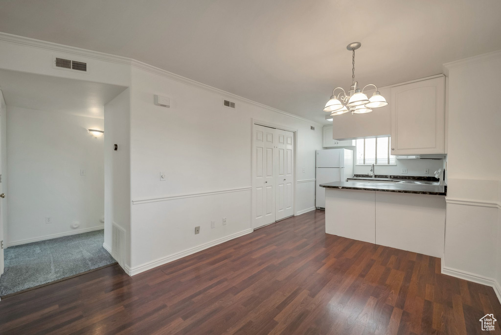 Kitchen with freestanding refrigerator, dark countertops, dark wood-style flooring, a peninsula, and ornamental molding