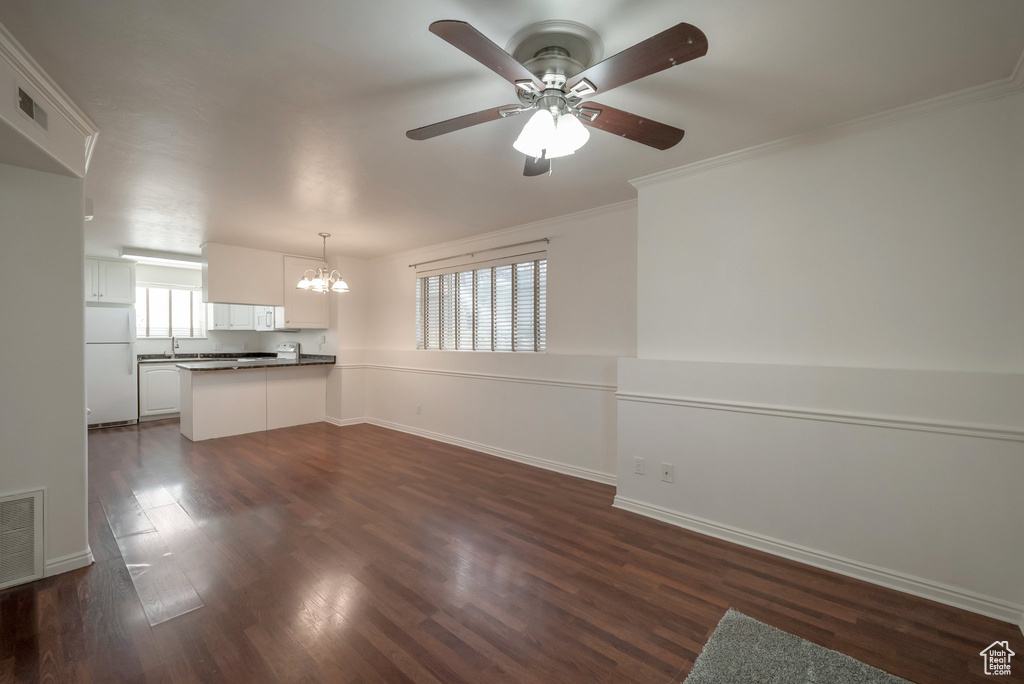 Unfurnished living room with a chandelier, a ceiling fan, dark wood finished floors, and ornamental molding