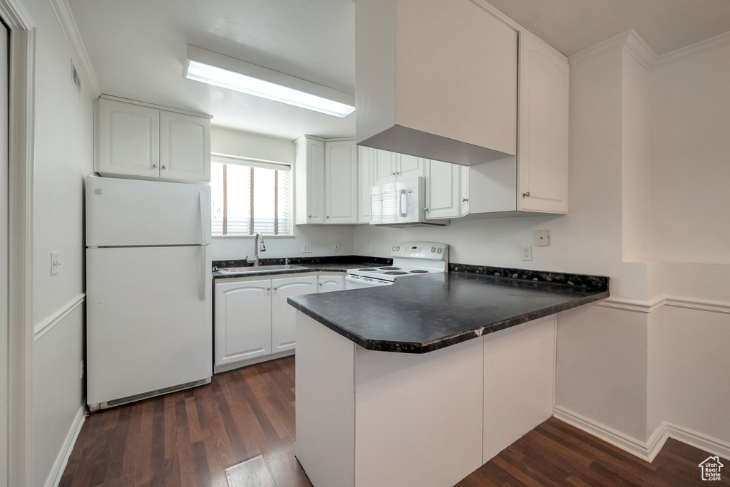 Kitchen featuring white appliances, a peninsula, dark countertops, dark wood-type flooring, and white cabinets