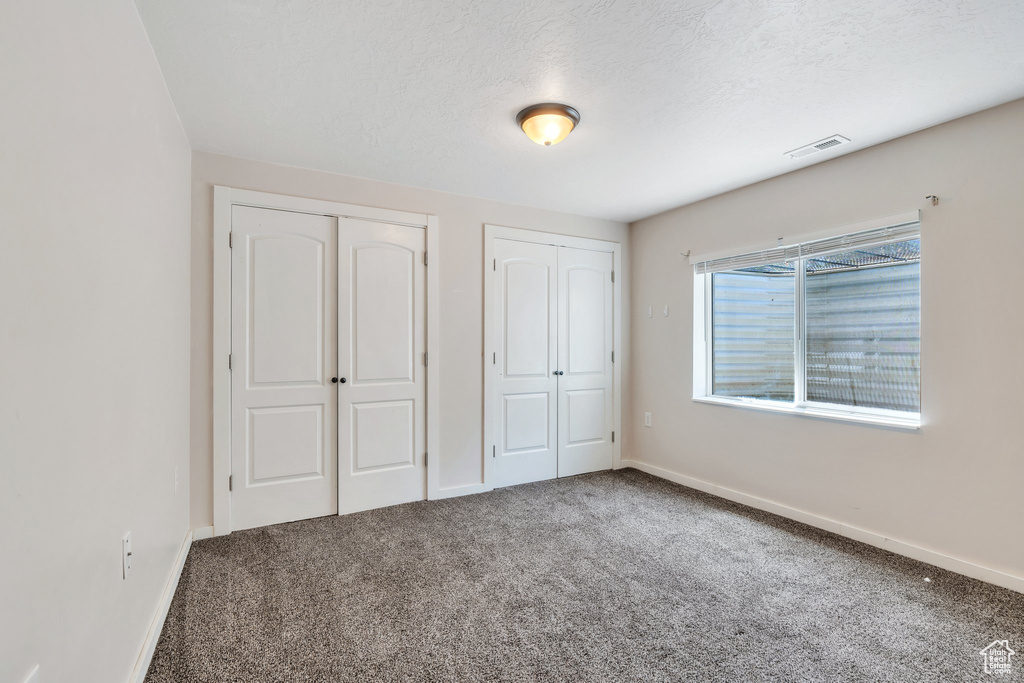 Unfurnished bedroom featuring multiple closets, carpet, and a textured ceiling