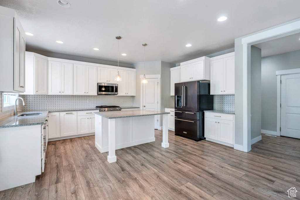 Kitchen featuring stainless steel microwave, black fridge with ice dispenser, range, decorative backsplash, and light wood-style floors