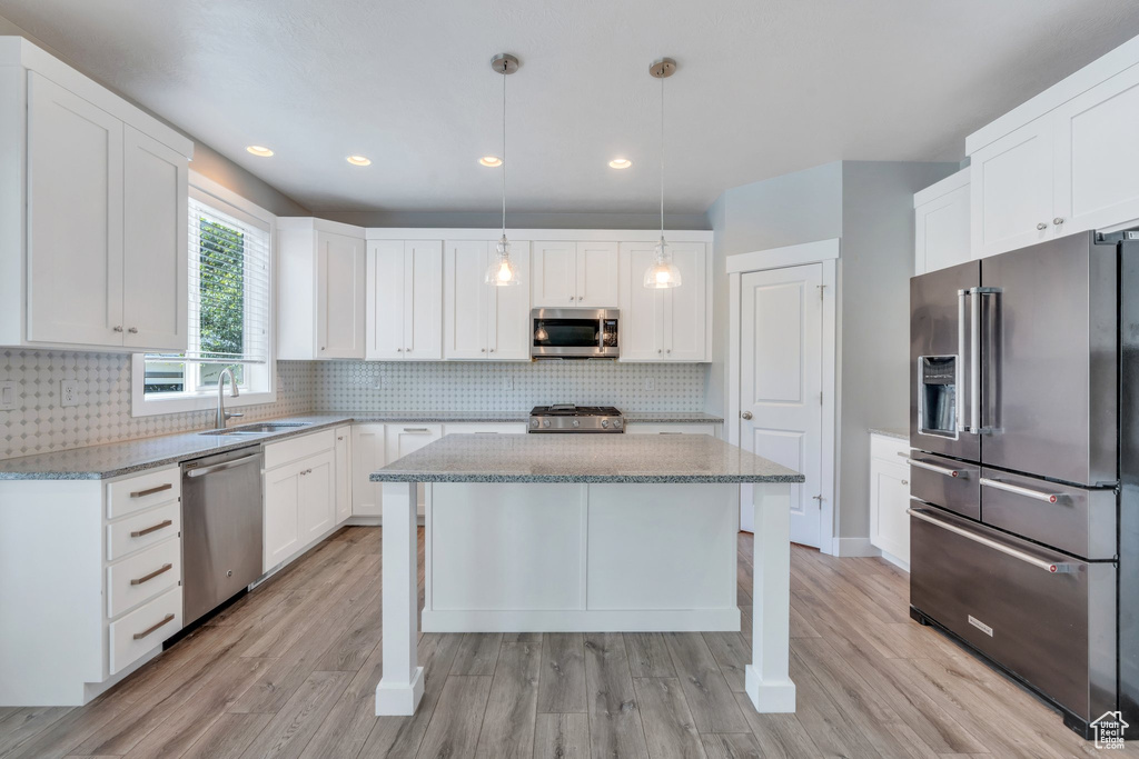 Kitchen with appliances with stainless steel finishes, light wood-style flooring, light stone countertops, a center island, and recessed lighting