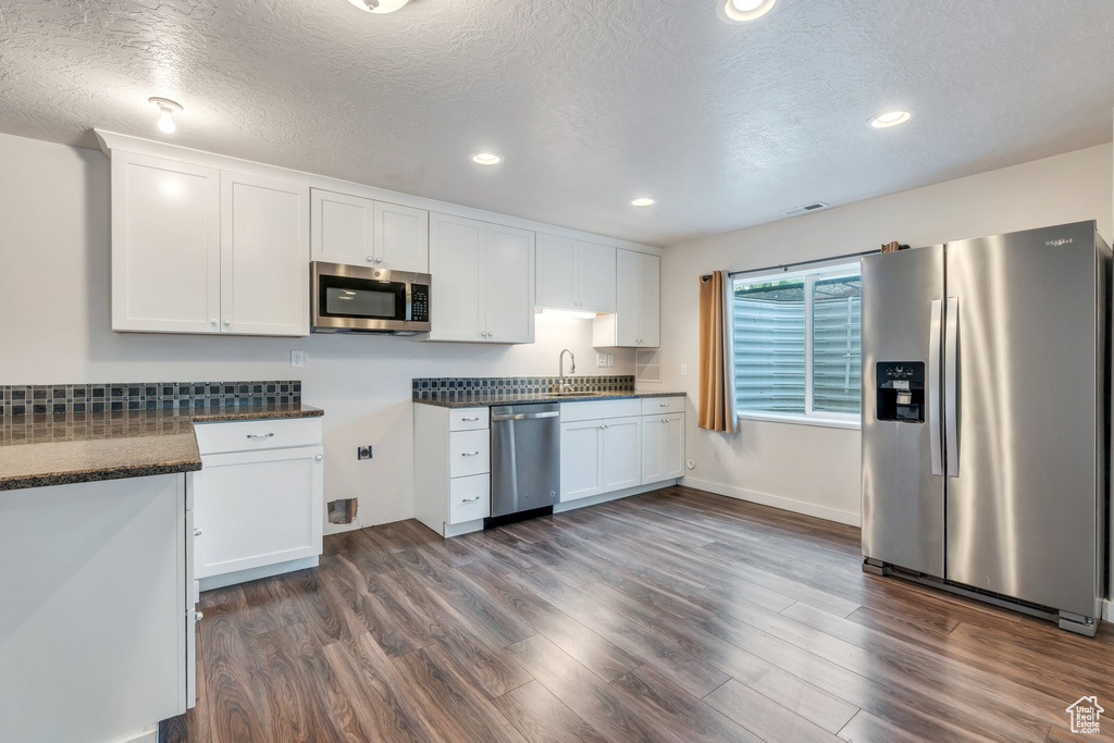 Kitchen with appliances with stainless steel finishes, white cabinetry, dark wood finished floors, recessed lighting, and a textured ceiling