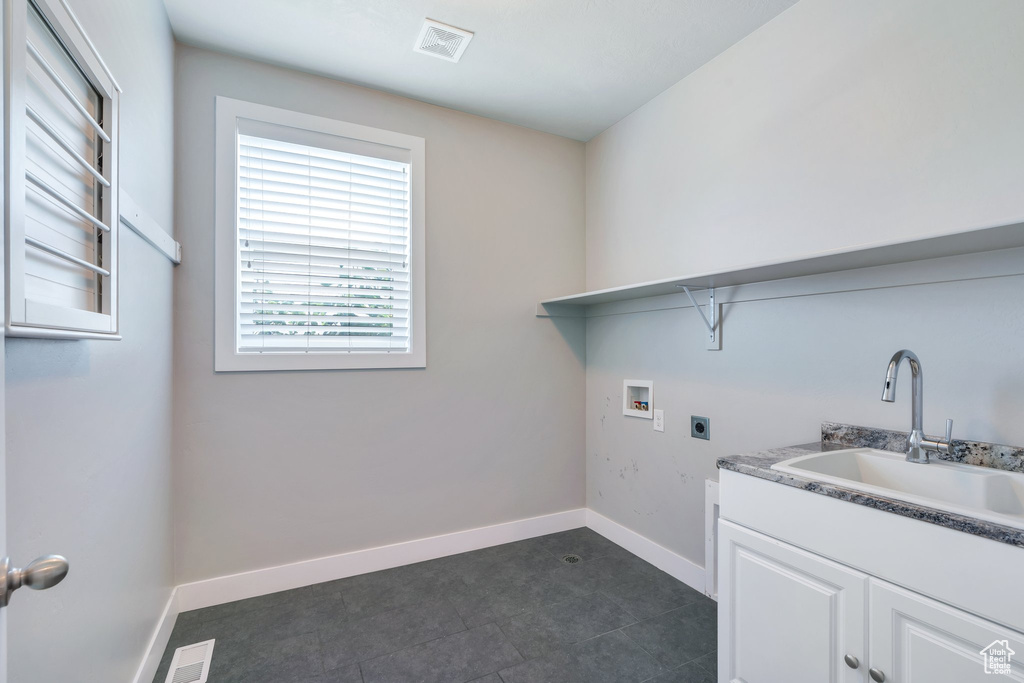Laundry area featuring electric dryer hookup, hookup for a washing machine, dark tile patterned floors, and cabinet space