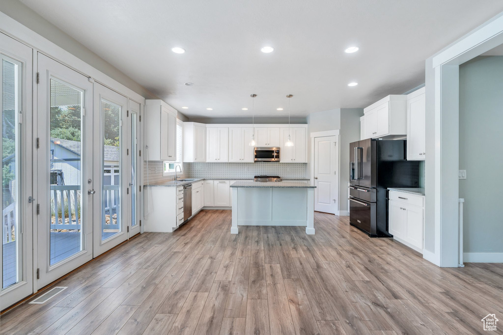 Kitchen featuring appliances with stainless steel finishes, light wood-style floors, backsplash, a kitchen island, and white cabinets
