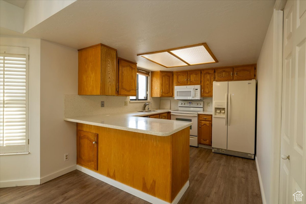 Kitchen with white appliances, brown cabinetry, a peninsula, and dark wood-style flooring