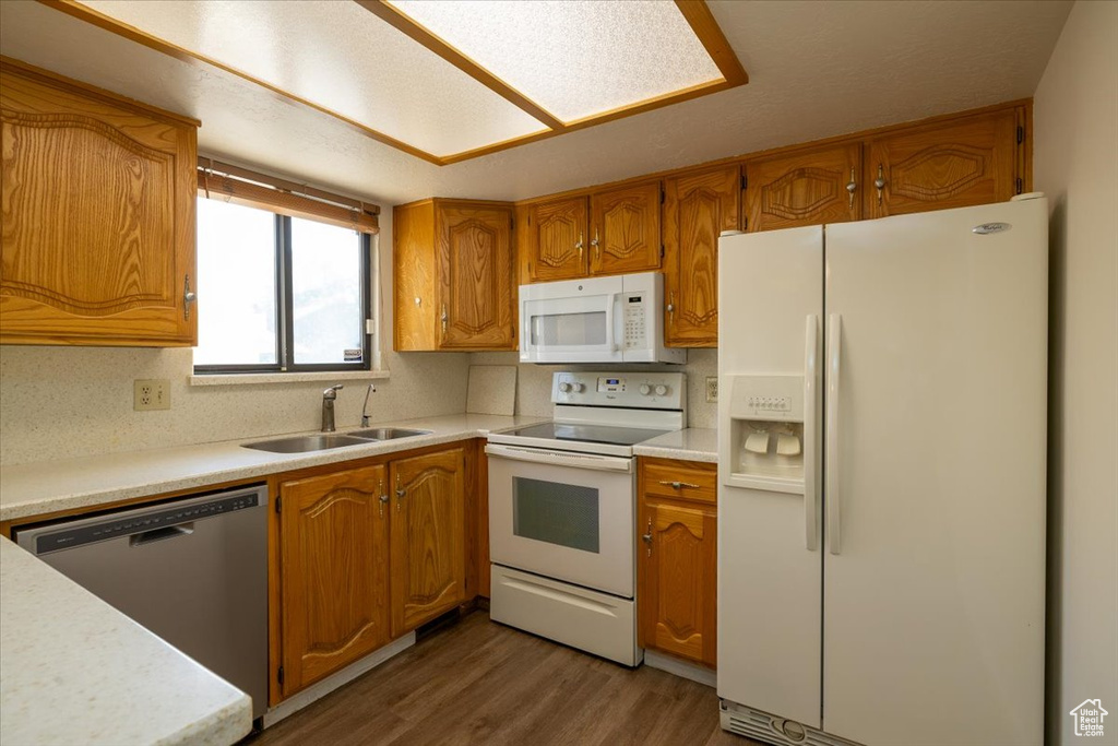 Kitchen featuring white appliances, brown cabinetry, wood finished floors, and light countertops