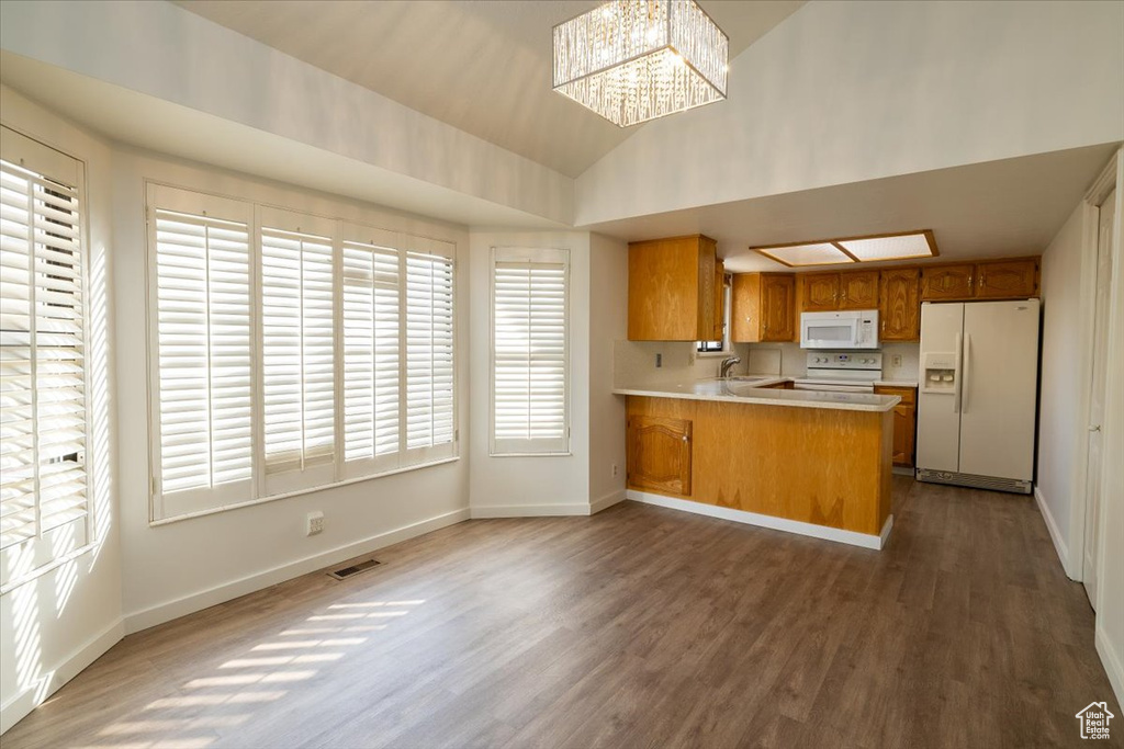Kitchen featuring white appliances, brown cabinetry, wood finished floors, a peninsula, and light countertops