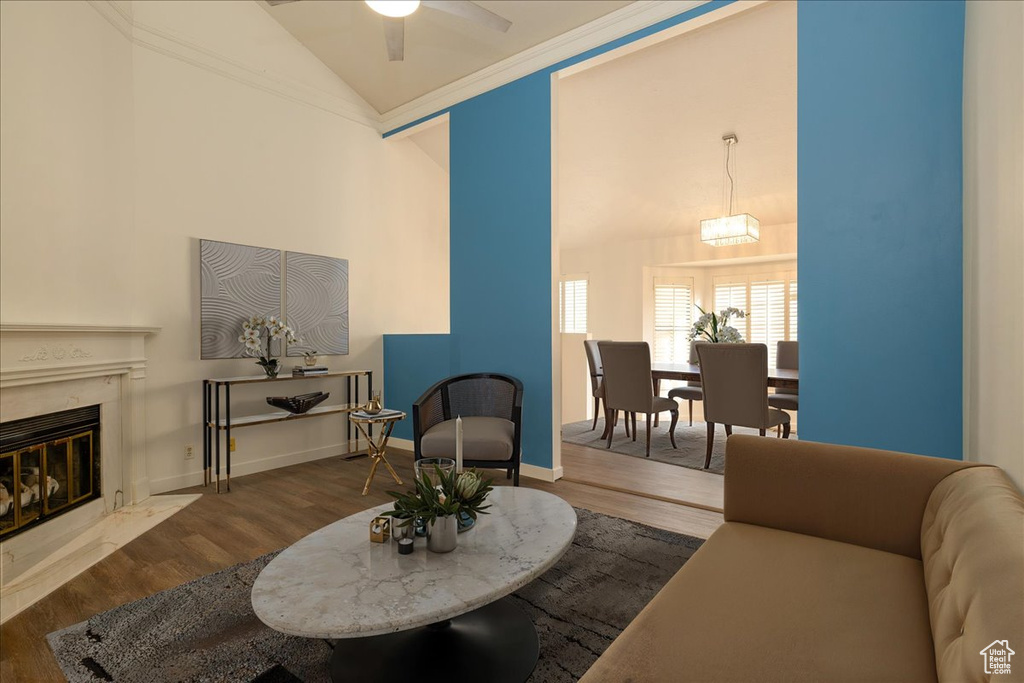 Living area with wood finished floors, a fireplace, a ceiling fan, ornamental molding, and high vaulted ceiling