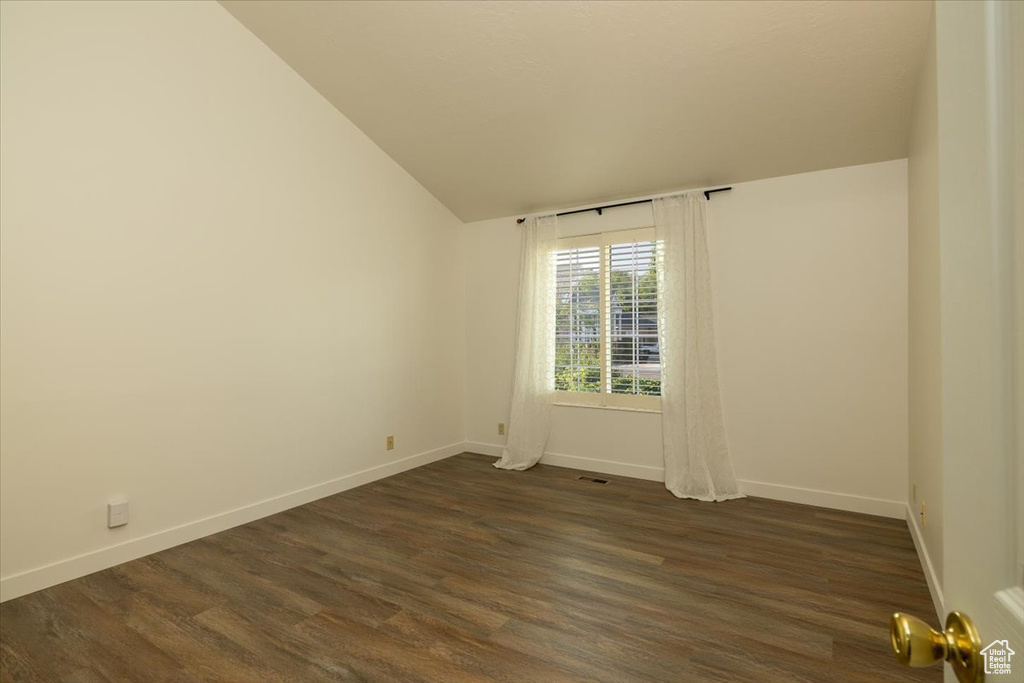 Spare room with dark wood finished floors and vaulted ceiling