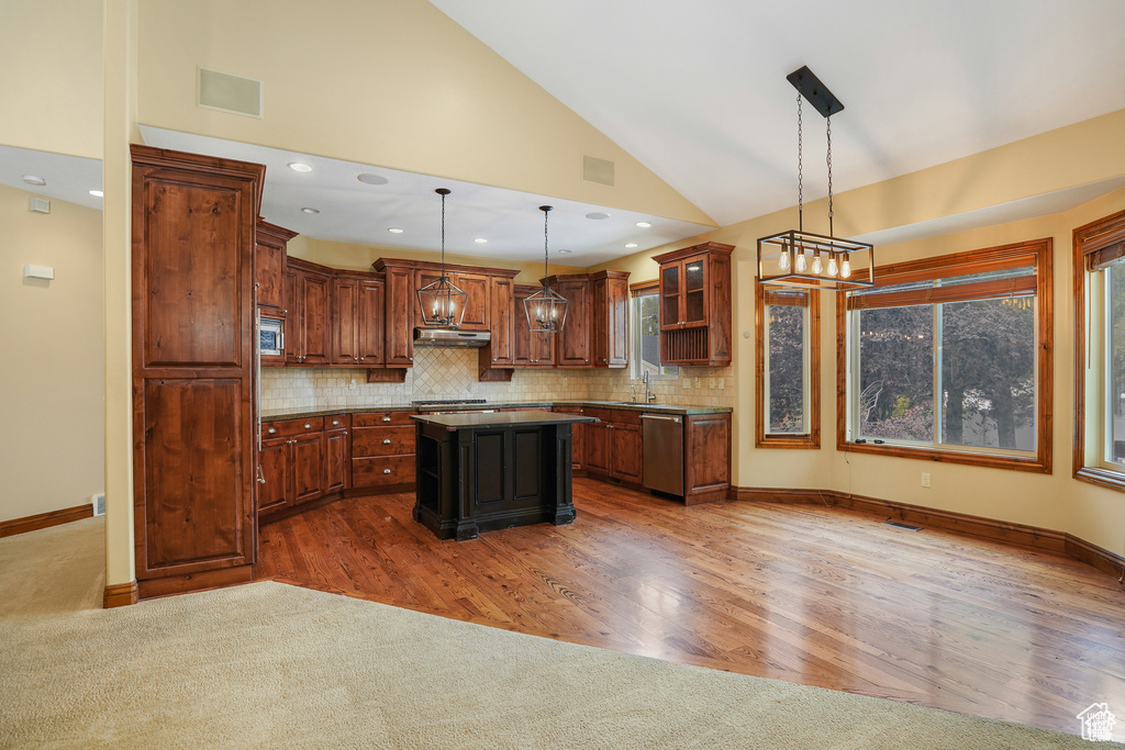 Kitchen featuring appliances with stainless steel finishes, decorative backsplash, a center island, decorative light fixtures, and glass insert cabinets