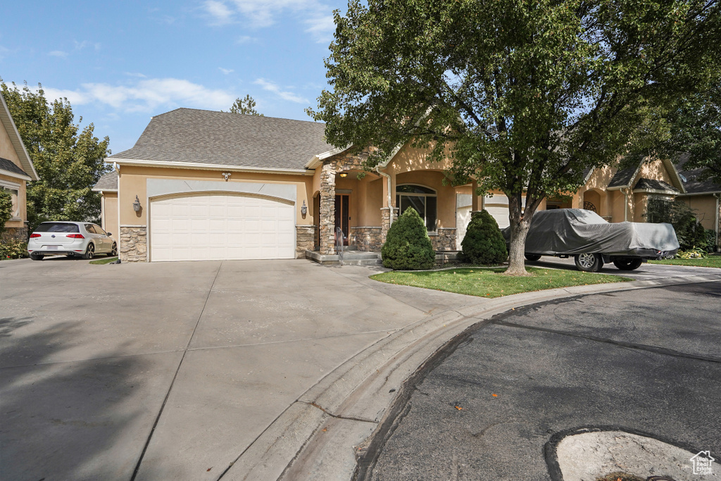 Obstructed view of property with driveway, stucco siding, stone siding, and an attached garage