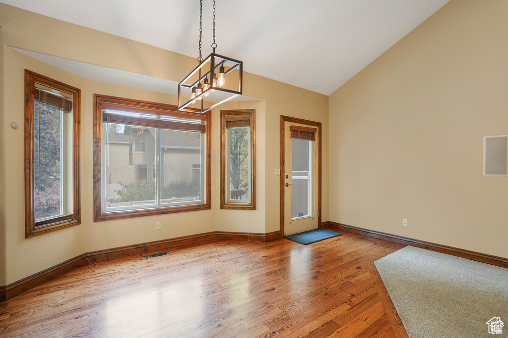 Unfurnished dining area with a chandelier, light wood-style flooring, and vaulted ceiling