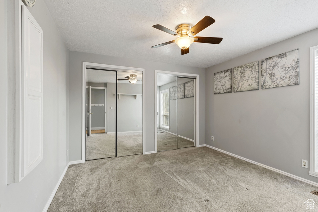 Unfurnished bedroom with two closets, carpet flooring, a textured ceiling, and ceiling fan