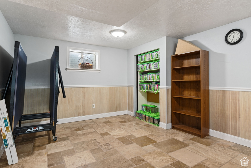 Workout room featuring stone tile floors, wainscoting, a textured ceiling, and wood walls