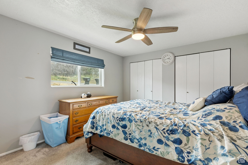Bedroom with light carpet, ceiling fan, and a textured ceiling