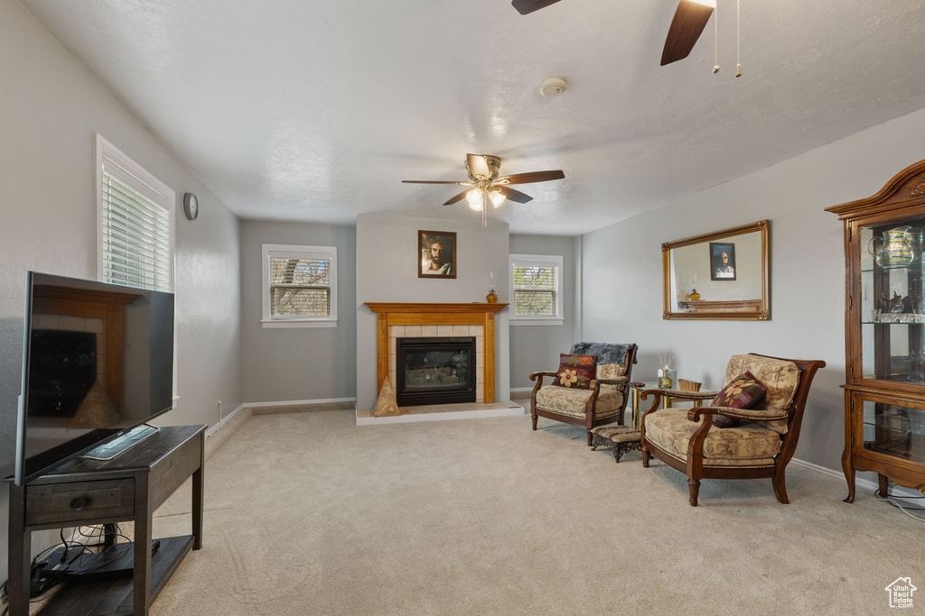 Living area with ceiling fan, light colored carpet, and a tiled fireplace
