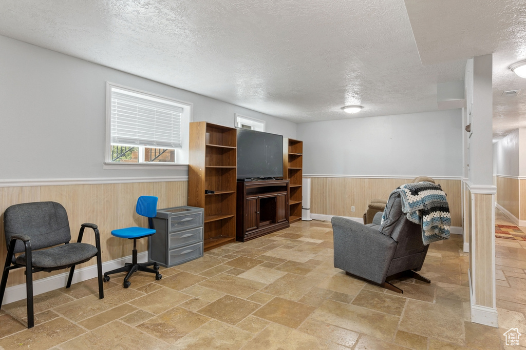 Living room featuring a textured ceiling, wainscoting, stone tile flooring, and wood walls
