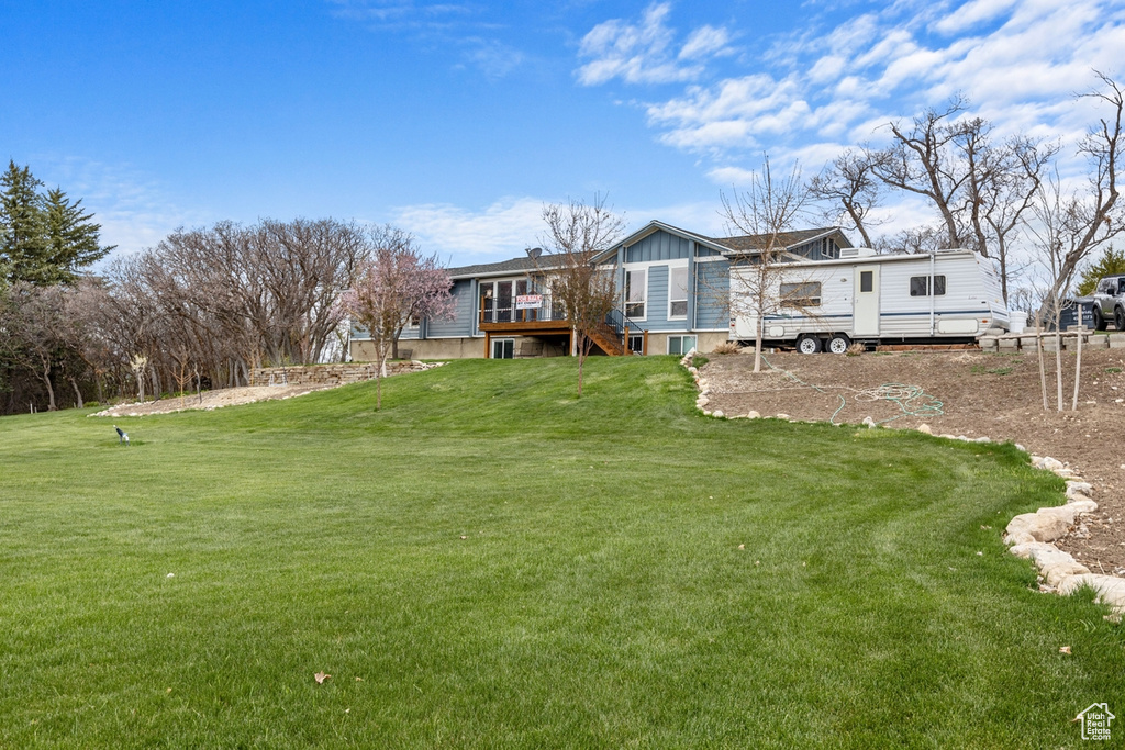 Rear view of property featuring a deck, stairway, a lawn, and board and batten siding