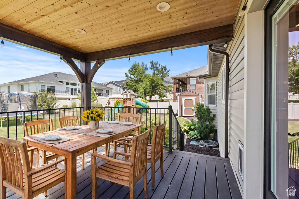 Deck featuring a playground, a shed, a residential view, outdoor dining area, and a fenced backyard