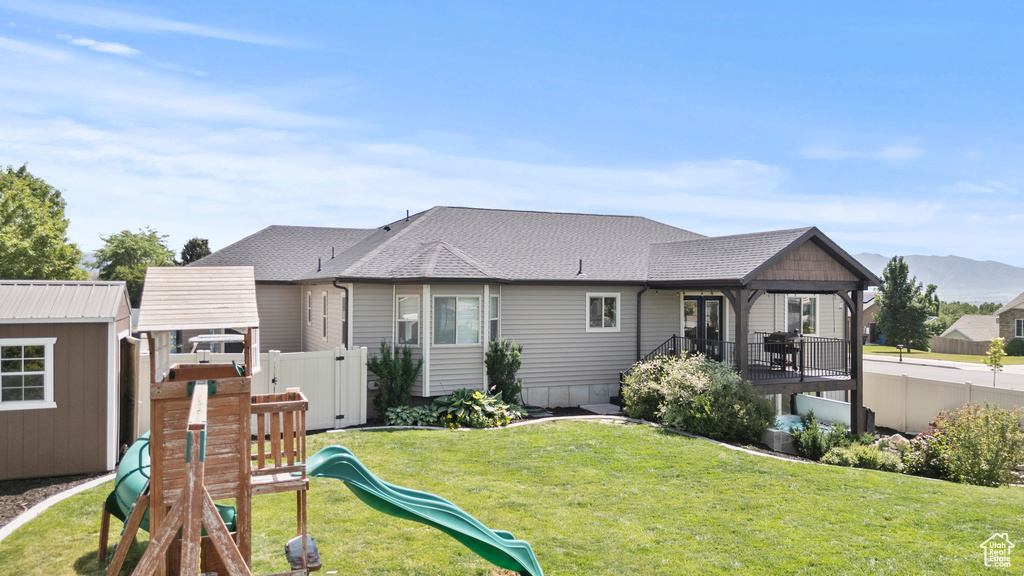 Rear view of house featuring a playground, roof with shingles, an outdoor structure, and a mountain view