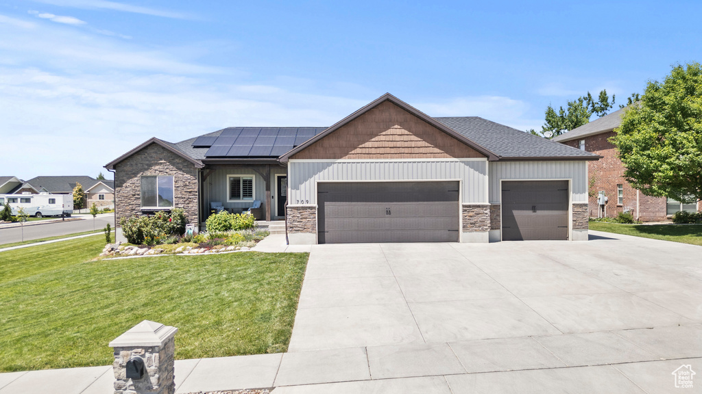 View of front of property featuring a garage, stone siding, a front yard, and roof mounted solar panels