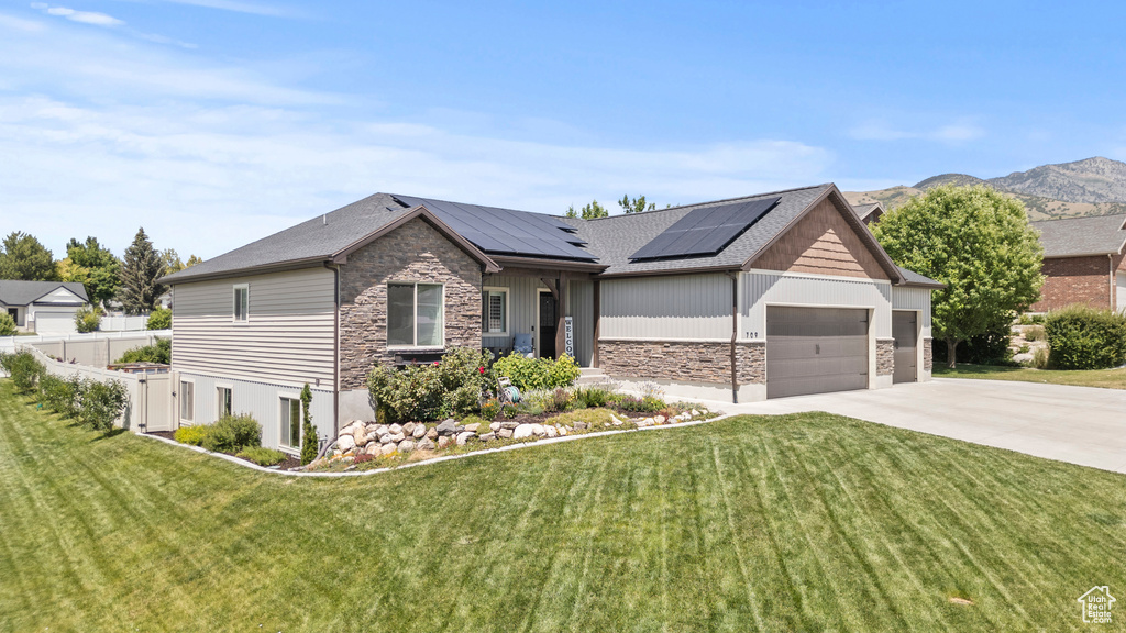 View of front of home with stone siding, an attached garage, driveway, and solar panels