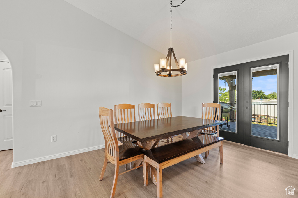 Dining area with lofted ceiling, french doors, light wood-style floors, arched walkways, and a chandelier