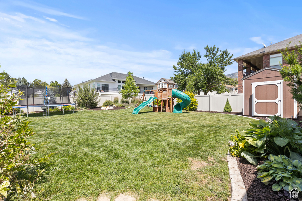 Fenced backyard featuring a trampoline, a shed, and a playground