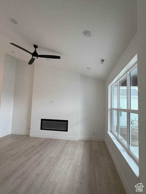 Unfurnished living room featuring a glass covered fireplace, light wood-type flooring, and a ceiling fan