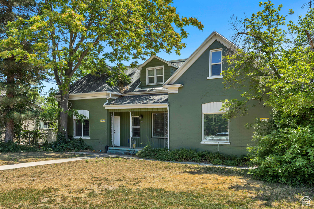 View of front of house featuring covered porch, a front lawn, a shingled roof, and brick siding