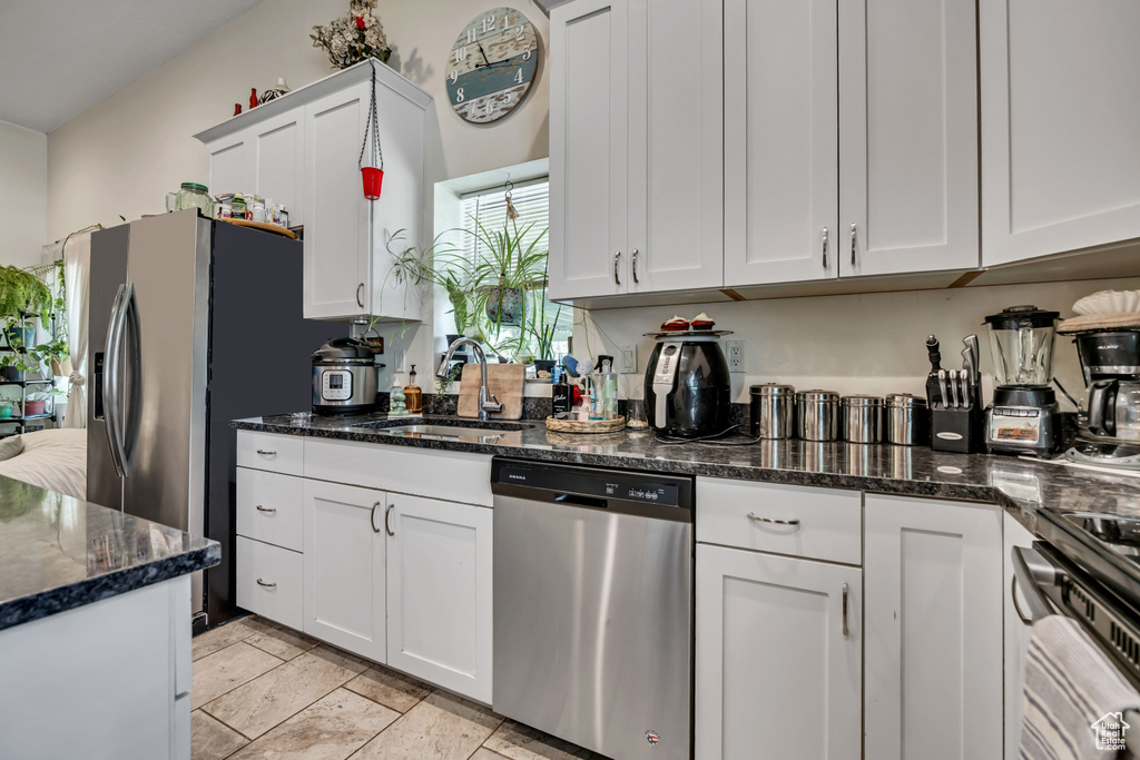 Kitchen with appliances with stainless steel finishes, white cabinets, and dark stone counters