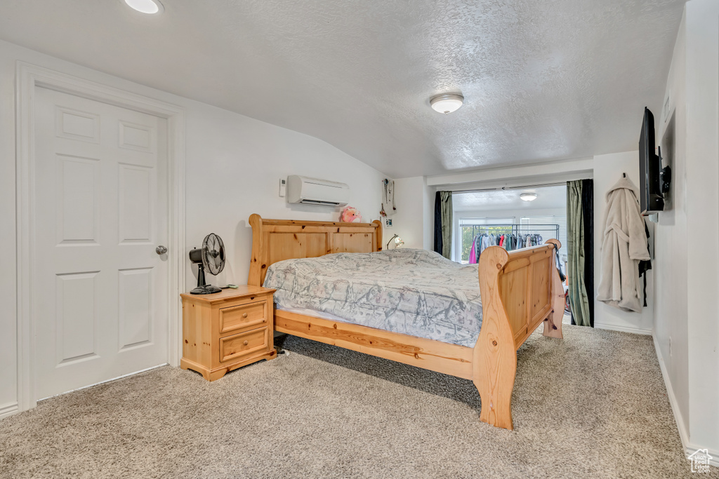 Carpeted bedroom with a wall mounted AC, a textured ceiling, and lofted ceiling