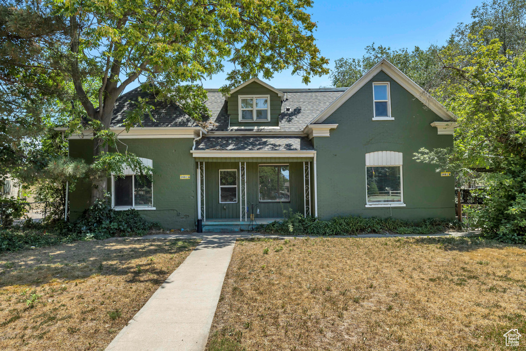 View of front of house with covered porch, roof with shingles, and a front yard