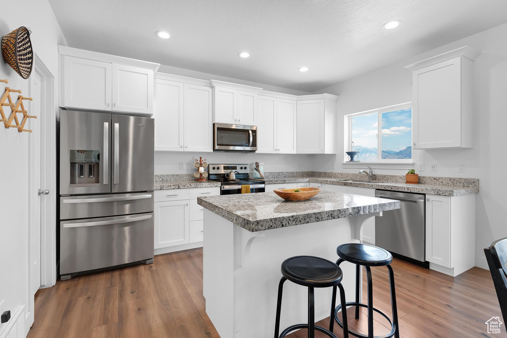 Kitchen with stainless steel appliances, dark wood finished floors, recessed lighting, white cabinets, and a center island