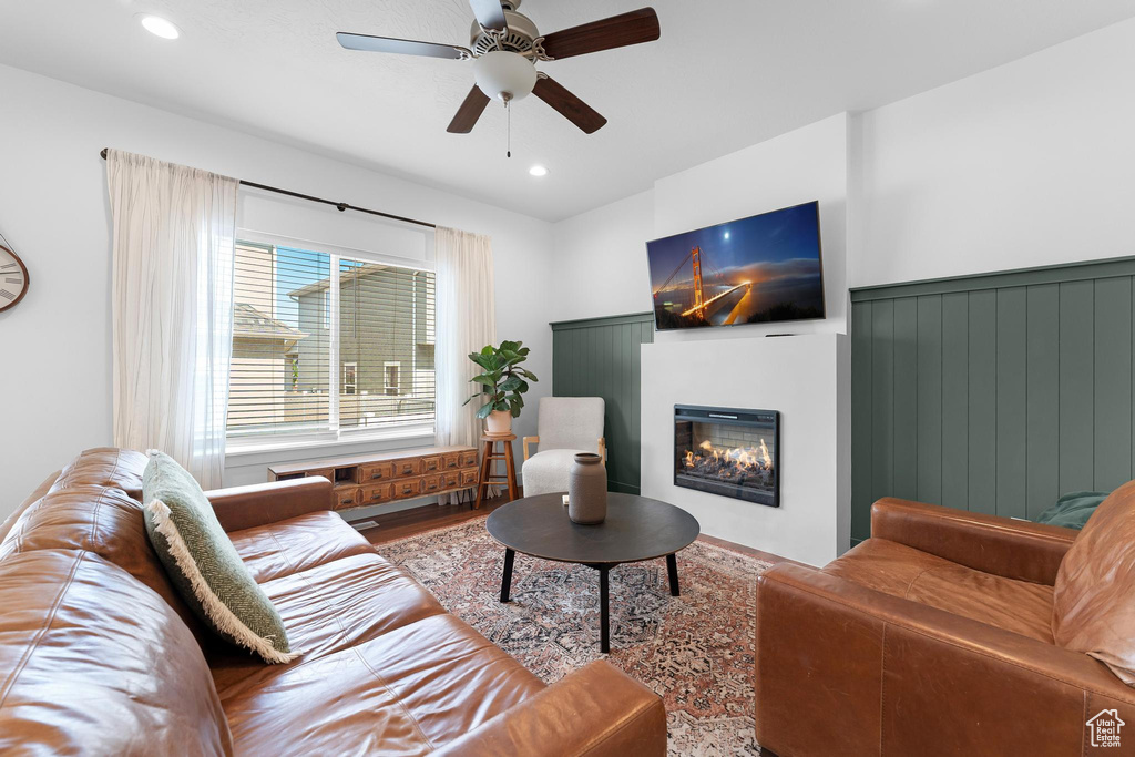 Living room with ceiling fan, a glass covered fireplace, wood finished floors, and recessed lighting