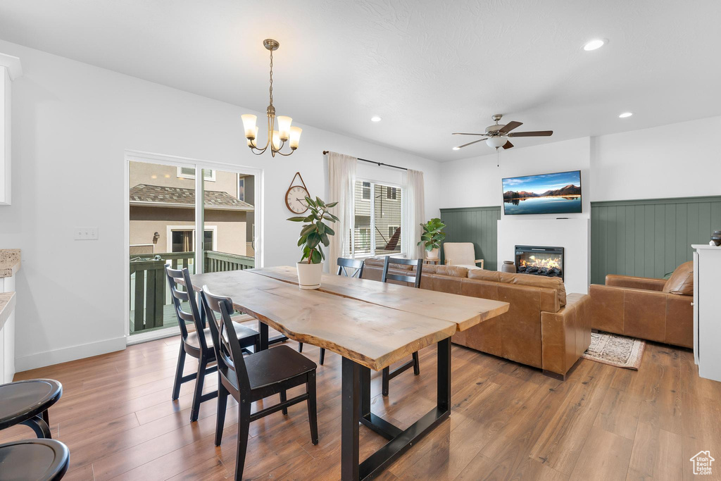Dining area with a ceiling fan, a glass covered fireplace, light wood-style floors, recessed lighting, and wainscoting