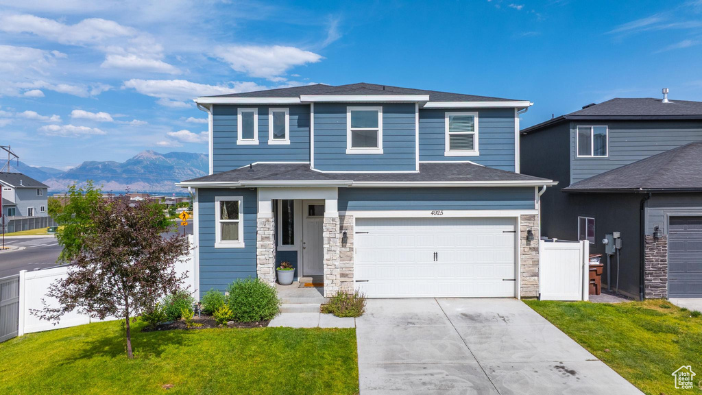 View of front facade featuring a mountain view, a garage, stone siding, and driveway