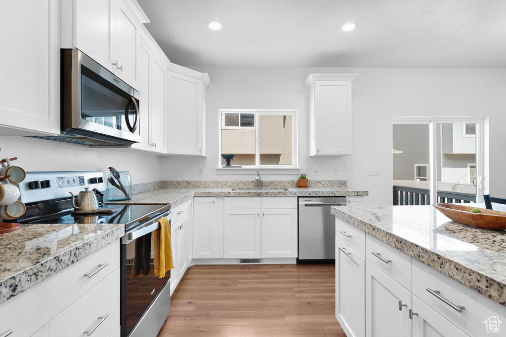 Kitchen with stainless steel appliances, white cabinetry, light wood finished floors, recessed lighting, and light stone countertops