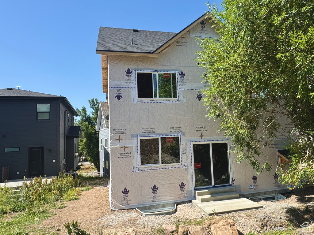 Back of property featuring entry steps, stucco siding, and roof with shingles