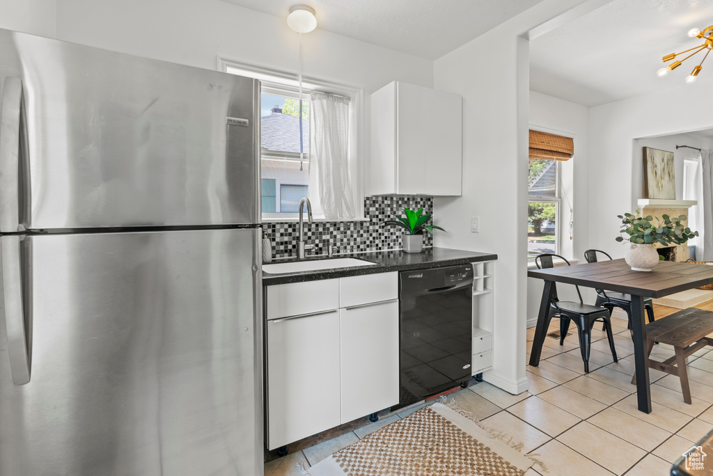 Kitchen with freestanding refrigerator, black dishwasher, dark countertops, decorative backsplash, and white cabinets