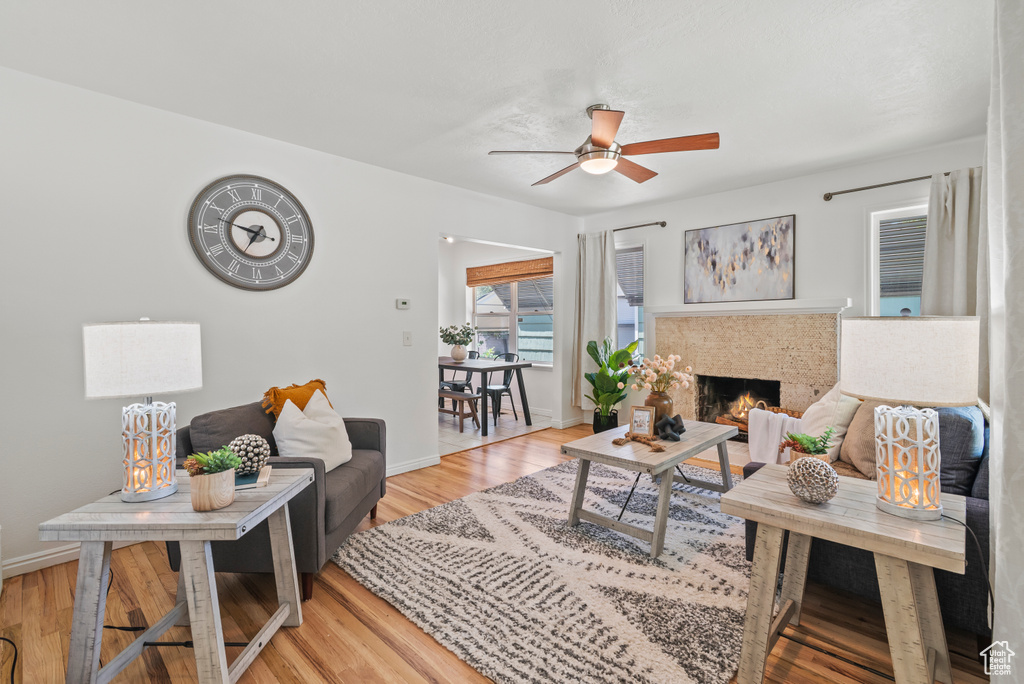 Living area featuring ceiling fan, light wood-style flooring, and a warm lit fireplace