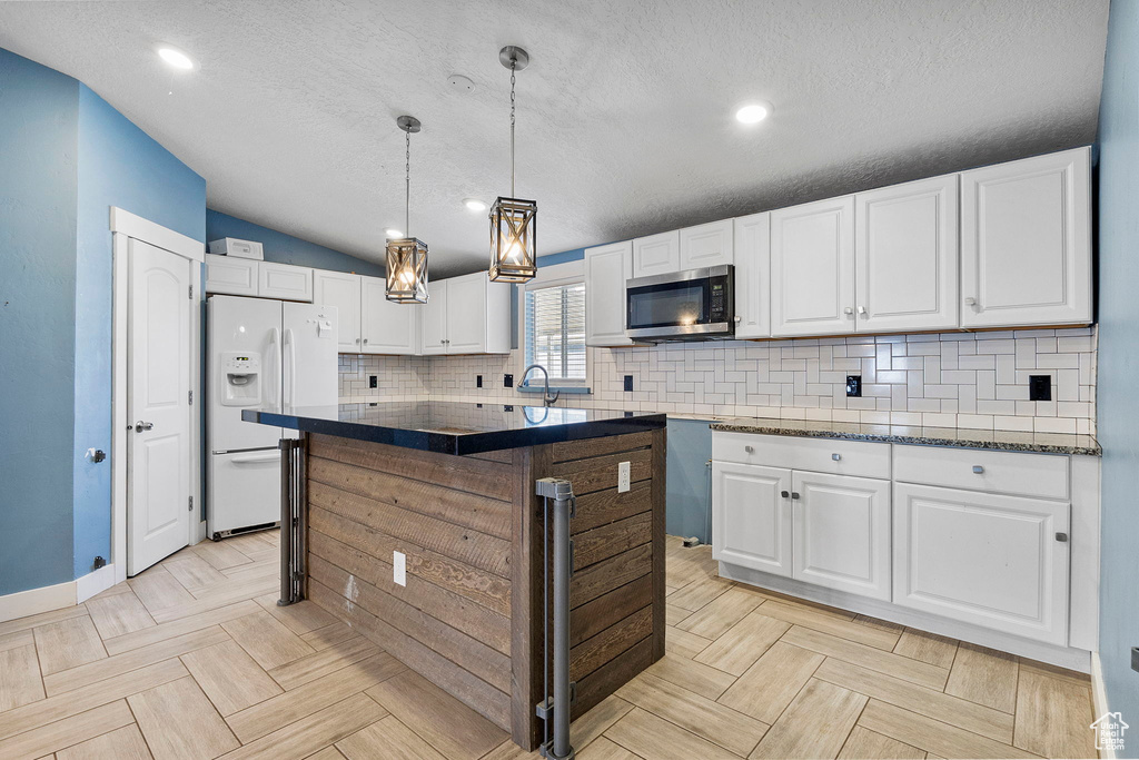 Kitchen featuring white fridge with ice dispenser, stainless steel microwave, tasteful backsplash, white cabinets, and a textured ceiling