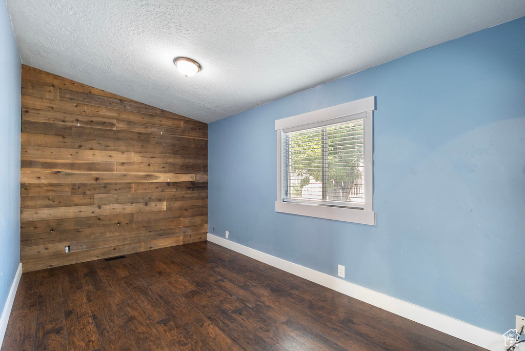 Empty room with lofted ceiling, dark wood-type flooring, and a textured ceiling