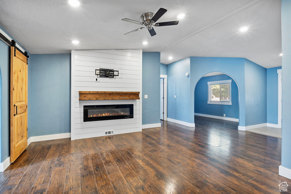 Unfurnished living room featuring a ceiling fan, a barn door, wood finished floors, a textured ceiling, and a large fireplace