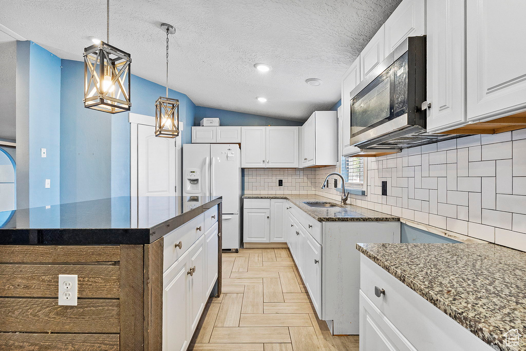 Kitchen featuring white refrigerator with ice dispenser, vaulted ceiling, stainless steel microwave, dark stone counters, and decorative backsplash