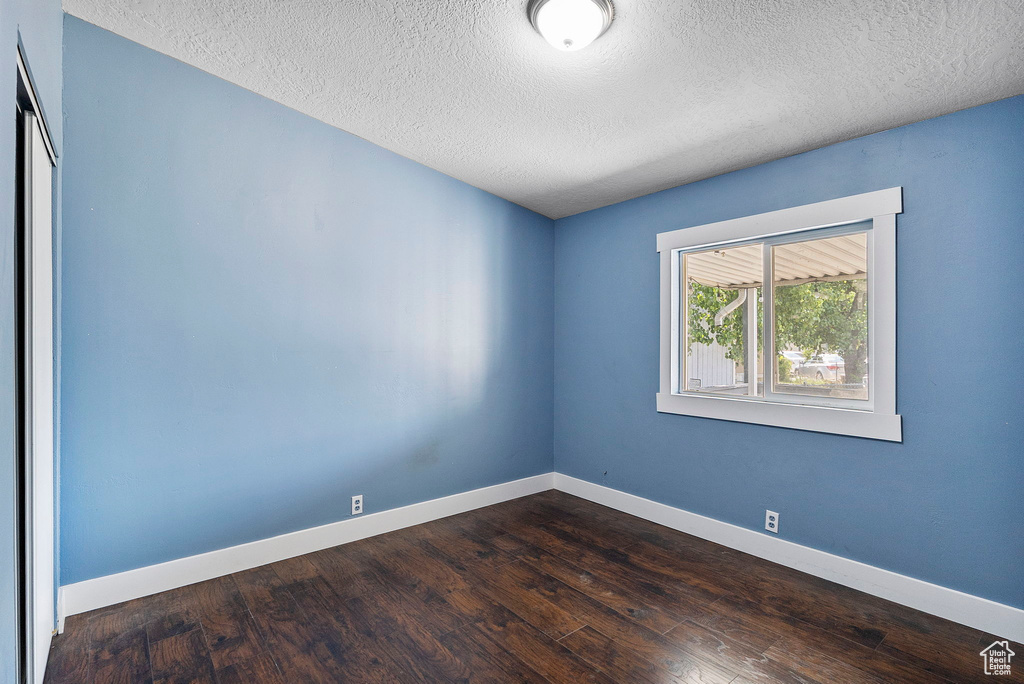 Empty room with a textured ceiling and dark wood-type flooring
