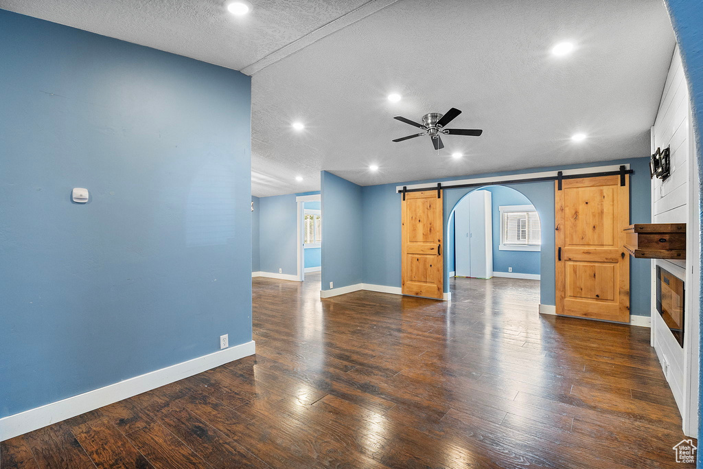 Unfurnished living room featuring a barn door, a ceiling fan, recessed lighting, wood finished floors, and a textured ceiling