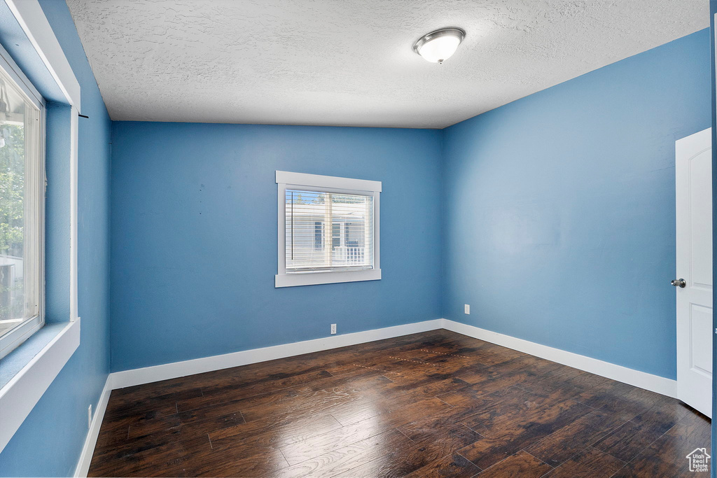 Empty room featuring healthy amount of natural light, dark wood finished floors, and a textured ceiling