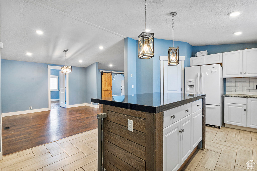Kitchen featuring white fridge with ice dispenser, a barn door, white cabinets, tasteful backsplash, and a kitchen island
